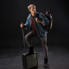 young student in a denim jacket and maroon sweater stands confidently in a studio, holding books...