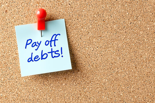 Debt payoff reminder: A blue sticky note pinned to a corkboard with handwritten encouragement to eliminate financial obligations.