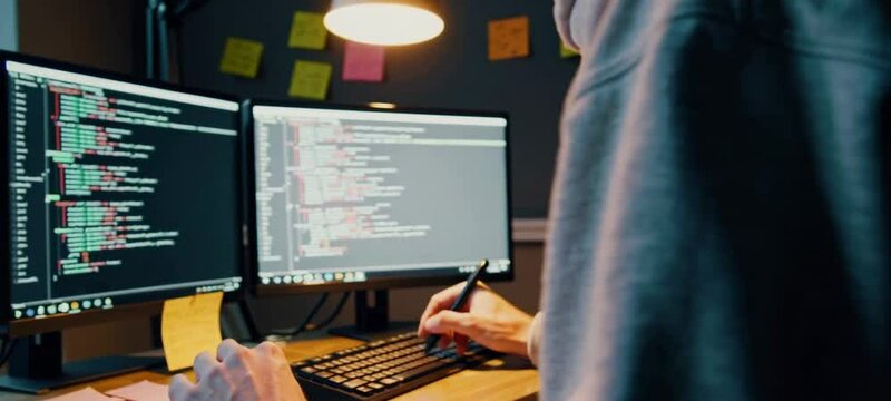Focused programmer writes and tests code in modern workspace with multiple monitors