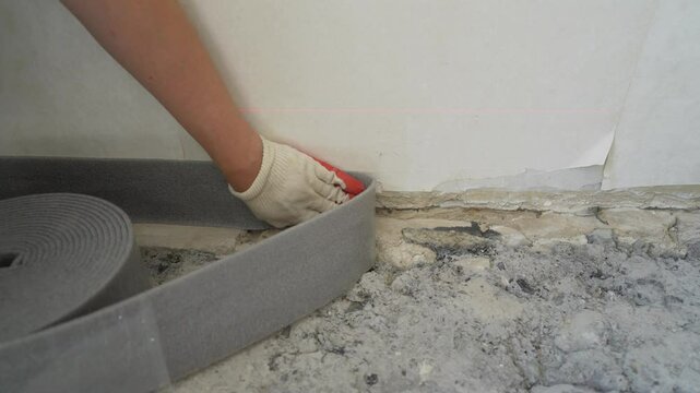 Construction professional installing soundproofing damping tape on interior wall, carefully measuring and applying insulation material during home renovation project