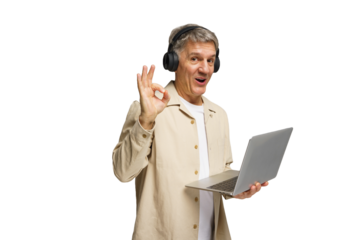 Senior man wearing headphones smiles while using a laptop in a bright setting during the day