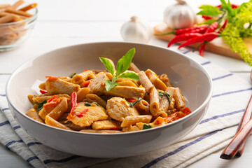 Stir fried whole wheat Penne rigate pasta with chicken breast in white plate.Pad Kra Pao,Thai fusion food.