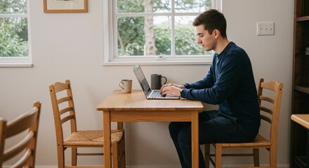 Young Man Working on Laptop in Cozy Modern Home Office with Coffee and Natural Light