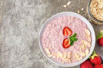 Strawberry oatmeal porridge in a bowl with fresh berries, almonds and mint on rustic concrete background. Top view with copy space. Healthy breakfast. Healthy eating and wellness, vegan food