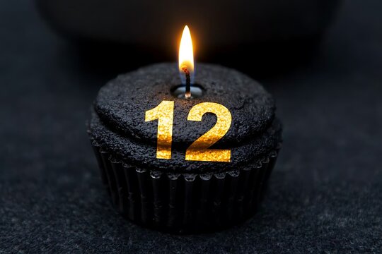 Lit twelve candle cupcake on dark surface