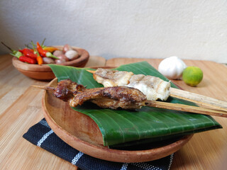 Fish satay with bamboo skewers on banana leaf and spices with wooden background 