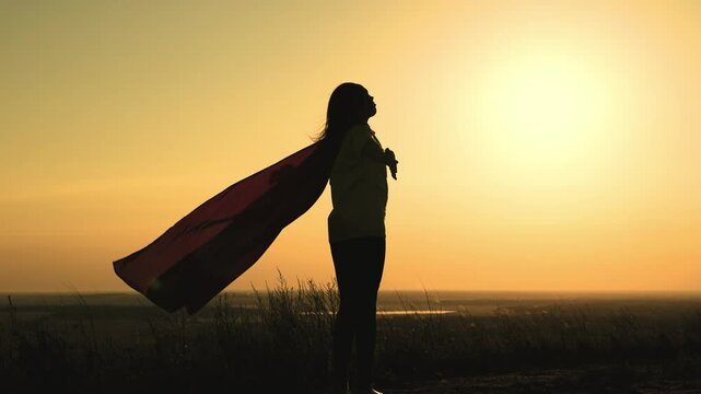 girl superhero with long hair red cape wind sunset. brave superhero ready help. superhero background sky rays sun. childhood dream teenager. child stretches hands sun. happy childhood superhero game.
