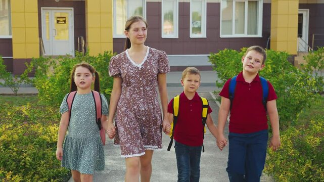 Mother leading children from school, female mother holding children hand, happy family, young nanny with children, schoolchildren with backpacks walking with aunt by the hand, little boys girl walking