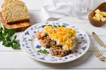 Shepherd's Pie or Cottage Pie on white plate. Savory pie made with beef mince and vegetables topped with mashed potatoes and cheese