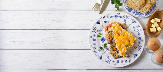 Shepherd's Pie or Cottage Pie on white plate. Savory pie made with beef mince and vegetables topped with mashed potatoes and cheese. View from above, top view with copy space