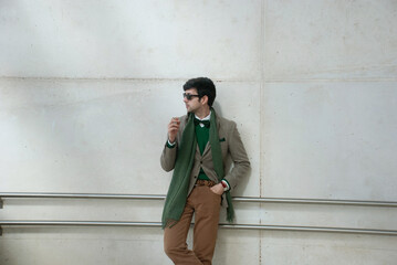 Hombre joven vestido con americana y bufanda posando fumando un cigarrillo con estilo en un...