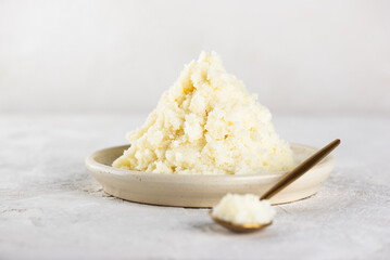 Unrefined shea butter in a plate and spoon on light table.