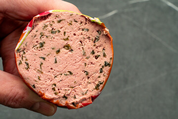 Hand is holding liverwurst with herbage. Dark marbled background.