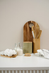 A curated collection of kitchen utensils and fresh ingredients: eggs, milk, sugar, cutboard, napkin is elegantly displayed on a neutral white table.