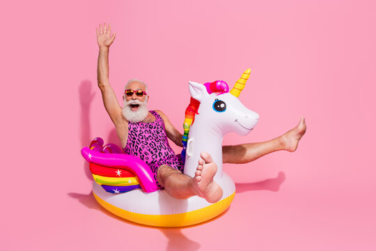 Elderly man in leopard print bodysuit enjoying a fun moment on unicorn float against vibrant pink background