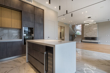Modern design of a luxury mansion with an installed kitchen set. Living room area with fireplace decorated with white marble tiles.