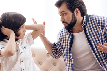 Grumpy father scolds son of teenager which plugs ears.