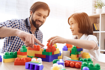Happy father and son play with colored plastic blocks.