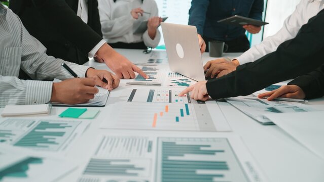 A diverse business team actively collaborating over charts and data in a modern office setting. Individuals engage with laptops, notepads, and digital tools for effective analysis. SACTR
