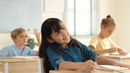 Smart elementary student looking at teacher while attend in classroom. Diverse smart student sitting at classroom while listening teacher explain about classwork or test. Education concept. Pedagogy.