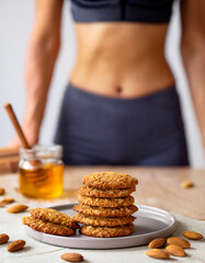 Assiette de biscuits croustillants aux flocons d&rsquo;avoine et au miel, avec amandes et une jeune femme sportive en arri&egrave;re-plan