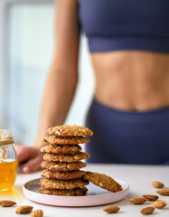 Pile de biscuits croustillants aux flocons d&rsquo;avoine et au miel, avec amandes et ventre plat d'une sportive en arri&egrave;re-plan