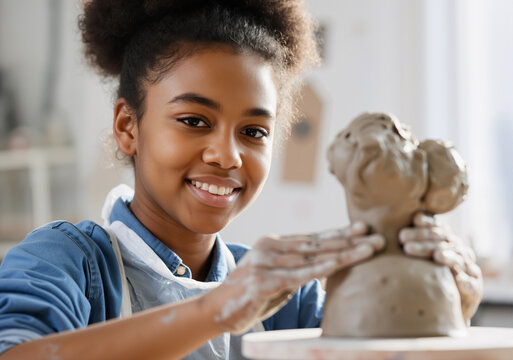 Smiling girl working on a clay bust in a pottery studio, enjoying her creative hobby