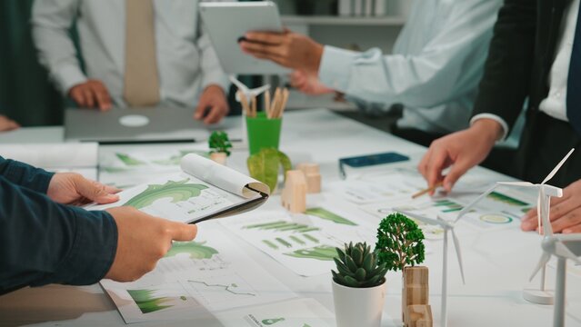 A diverse business team engaged in a collaborative meeting, analyzing environmental charts and graphs to develop sustainable strategies in a modern office setting. SACTR