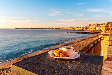 concept of street outdoor breakfast with a cup of tea or coffee on a morning coast during sunrise. landscape of city embarkment with sea water and cloudy sky on background