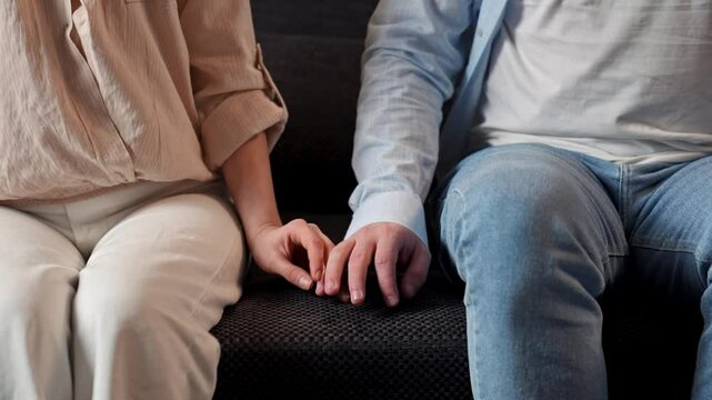 Lovely couple relaxing on the couch at home, close shot of man and woman sit on sofa and touching fingers and holding hands tight. Slow motion.