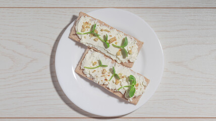 A pair of crispbread toasts with creamy cheese, walnut crumbles, and microgreens on a plate.