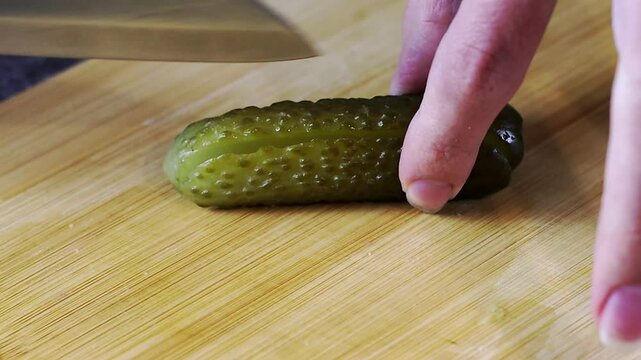A detailed closeup image of a hand skillfully slicing a pickle on a rustic wooden cutting board using a chefs knife