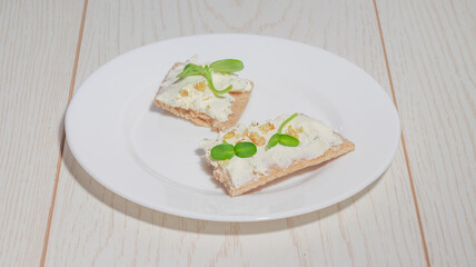 Detailed close-up of crispbread with a creamy spread, microgreens, and crushed nuts on a plate.