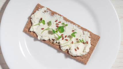Close-up of a crispbread with cream cheese, flax seeds, and microgreens on a plate.