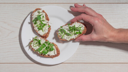 A white plate with three slices of bread topped with soft cheese and fresh microgreens, placed on a wooden table.
