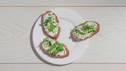 A top-down view of a white plate with three gourmet bruschetta, one of them slightly moved away, featuring creamy cheese and microgreens.