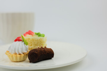 Side view of mini desserts lying on a plate, behind them is a white mug with a hot drink on a white background with space for text. The concept of mini desserts, sweets, confectionery. High quality
