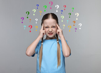 Little girl thinking hard surrounded by question marks on grey background