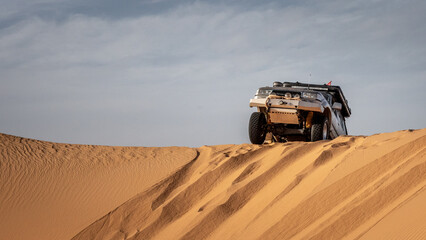 A 4x4 camper equipped with a roof tent crosses a sand dune of the Admer erg in the heart of the Algerian Sahara desert