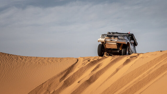 A 4x4 camper equipped with a roof tent crosses a sand dune of the Admer erg in the heart of the Algerian Sahara desert