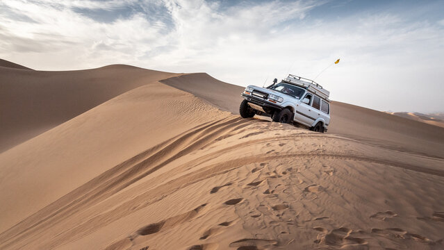 A 4x4 camper equipped with a roof tent crosses a sand dune of the Admer erg in the heart of the Algerian Sahara desert