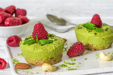 Matcha vegan cheesecakes with raspberries and mint on white plate with nuts and green tea powder. Raw vegan cakes with fresh berries. Healthy vegan dessert
