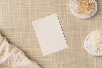 Paper blank sheet with fabric, ribbons and flowers on the table. Flat lay, top view.