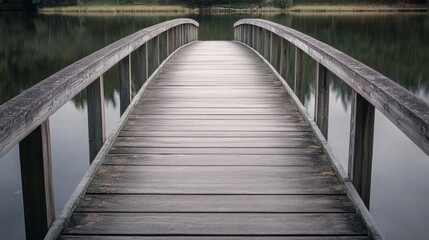 Obraz premium A weathered wooden bridge curves gently over calm waters, enveloped in serene natural surroundings, inviting reflection and peaceful passage.