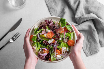 Plate of vegetable salad (Greek salad) with tomatoes, feta cheese, lettuce, olives and onions in hands
