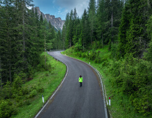 Woman walking on a winding mountain road in lush green forest on summer rainy day. Dolomites,...