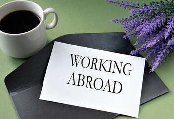 WORKING ABROAD - words on a white sheet on the background of a black envelope, a cup of coffee, and...