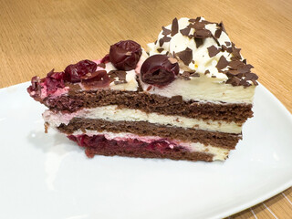 Slice of black forest cake with cherries and chocolate shavings on white plate
