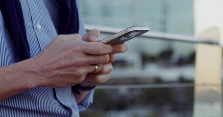 A man uses a mobile phone while standing outdoors. Close-up of his hands, unrecognizable persona
