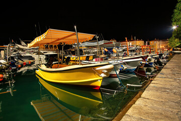 A peaceful night in Budva's lively harbor, filled with colorful boats and reflections.